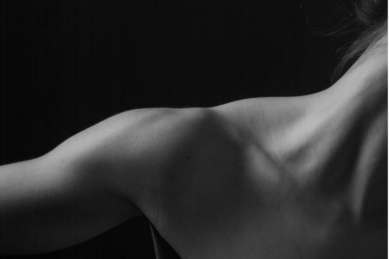 A bare back and shoulder in dramatic black and white studio light - no face visible